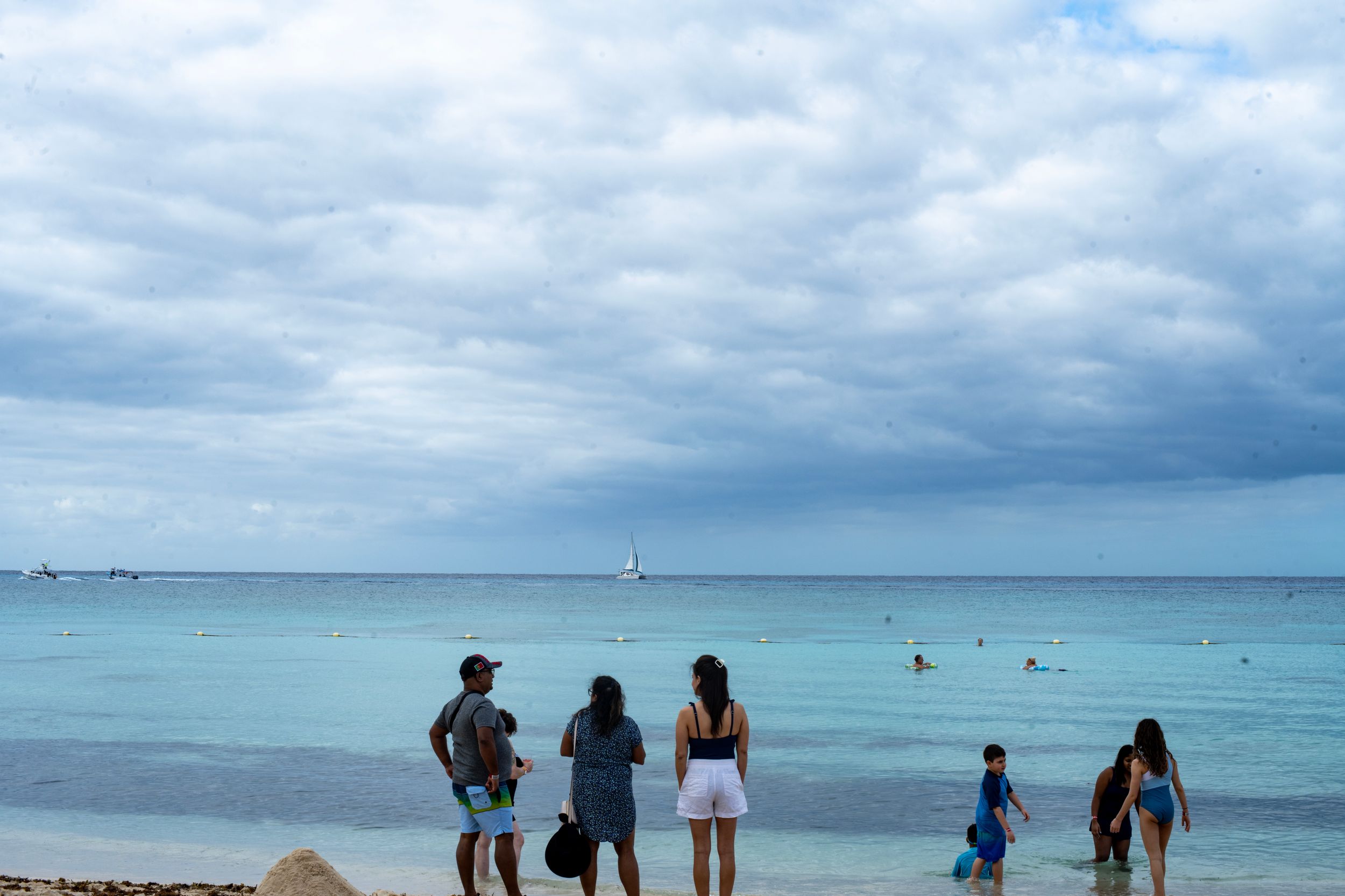 People standing on a tropical beach with turquoise water and dramatic cloudy skies overhead.