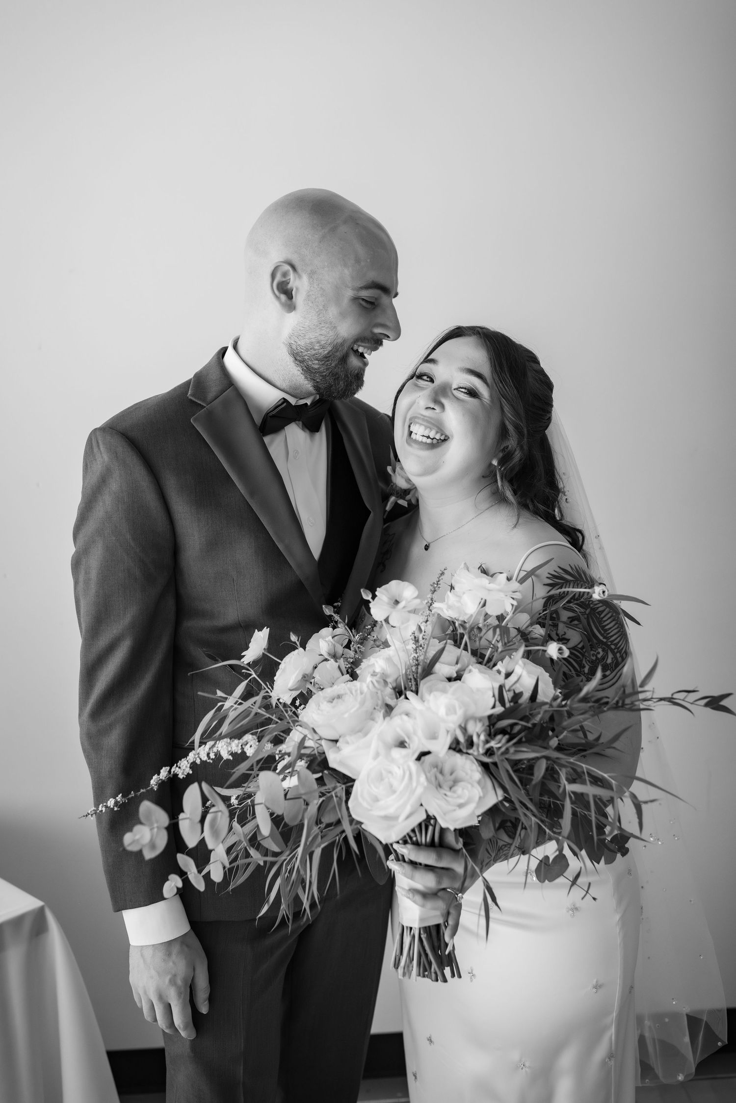 Black and white portrait of smiling bride and groom holding a floral wedding bouquet.