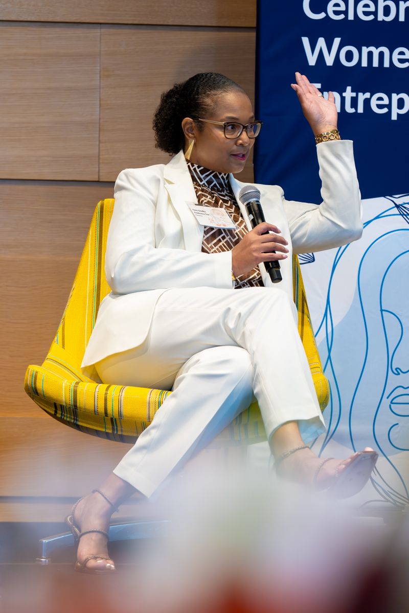 Professional event speakers seated at a panel discussion wearing white blazers and yellow chairs in a conference setting.