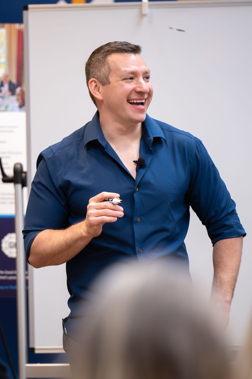 Smiling man in blue shirt holding a marker while presenting at a whiteboard during a business seminar.