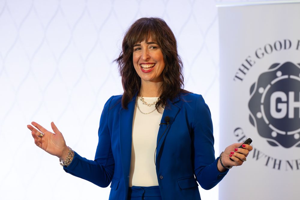 Woman in blue blazer presenting at The Good Growth Network conference, gesturing expressively on stage.