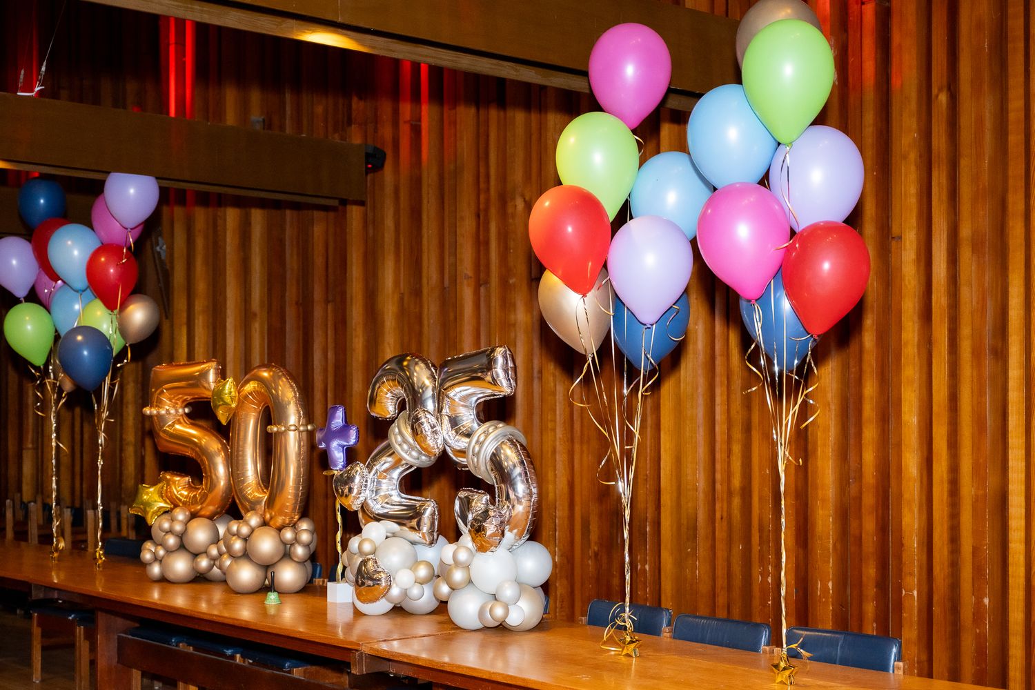 Gold and silver number balloons spelling 50 and 55 displayed on a stage with colorful balloon arrangements at a birthday party.