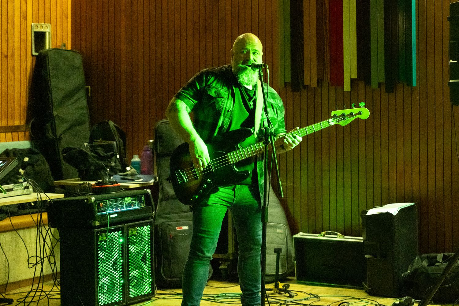 Musician playing bass guitar on stage under green lighting at an indoor venue.