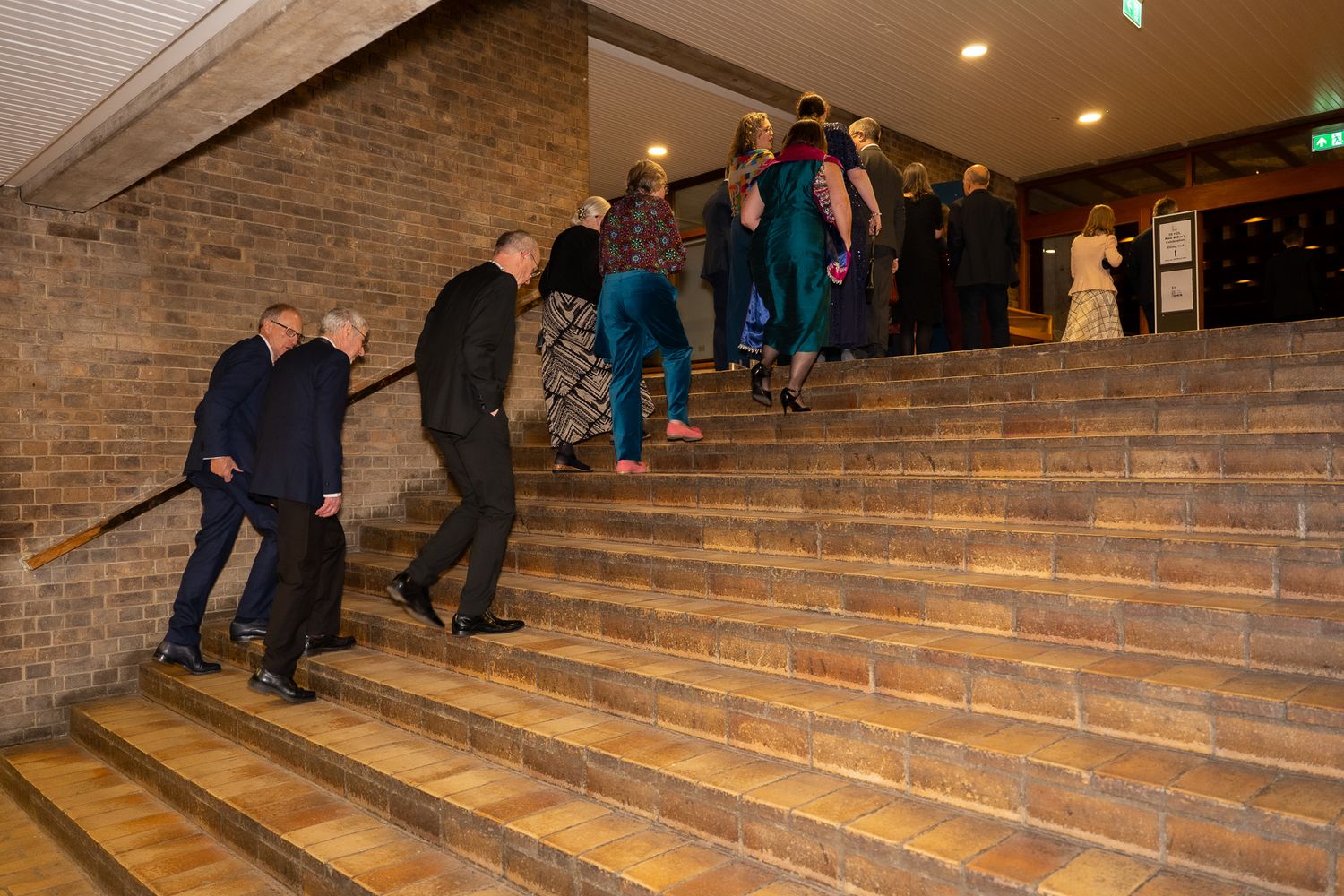 Elegantly dressed guests climb brick stairs at a formal evening event.