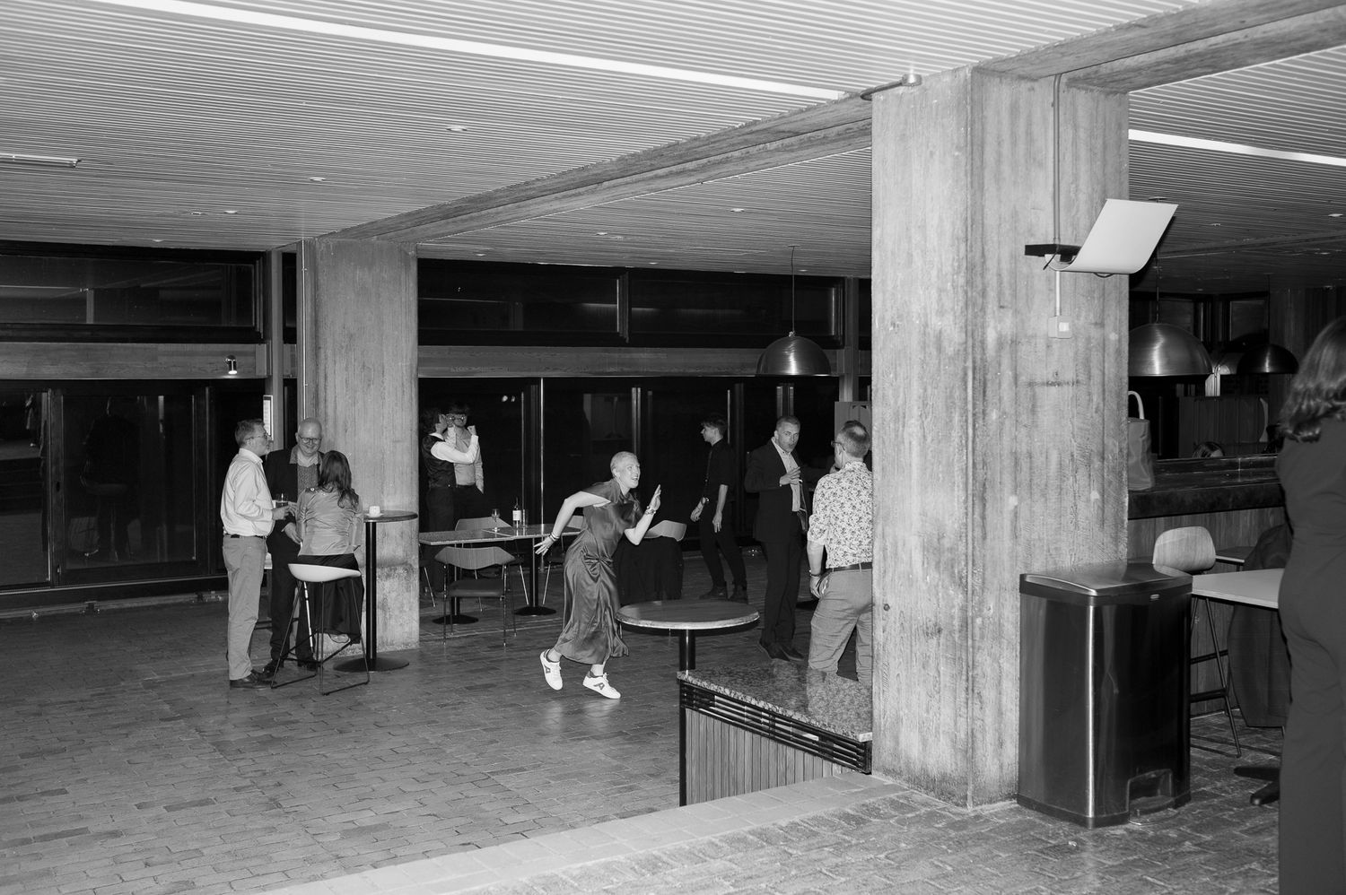 Black and white photo of people playing ping pong in a mid-century building lobby with concrete columns.