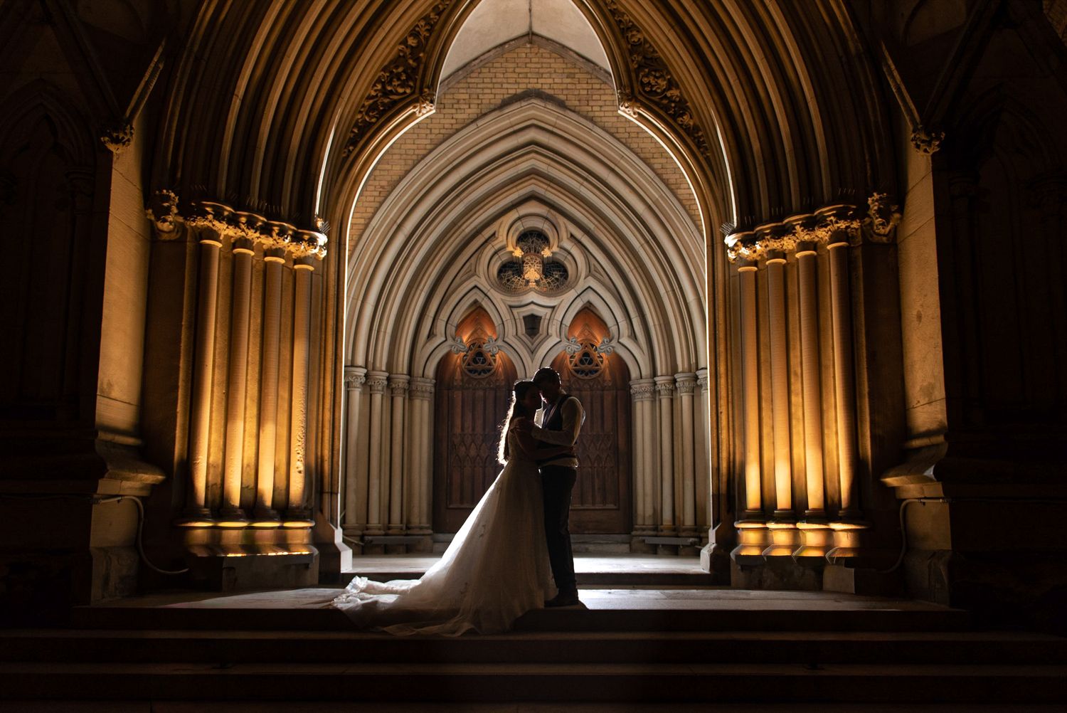 Couple silhouetted against stunning illuminated Gothic cathedral interior at night.