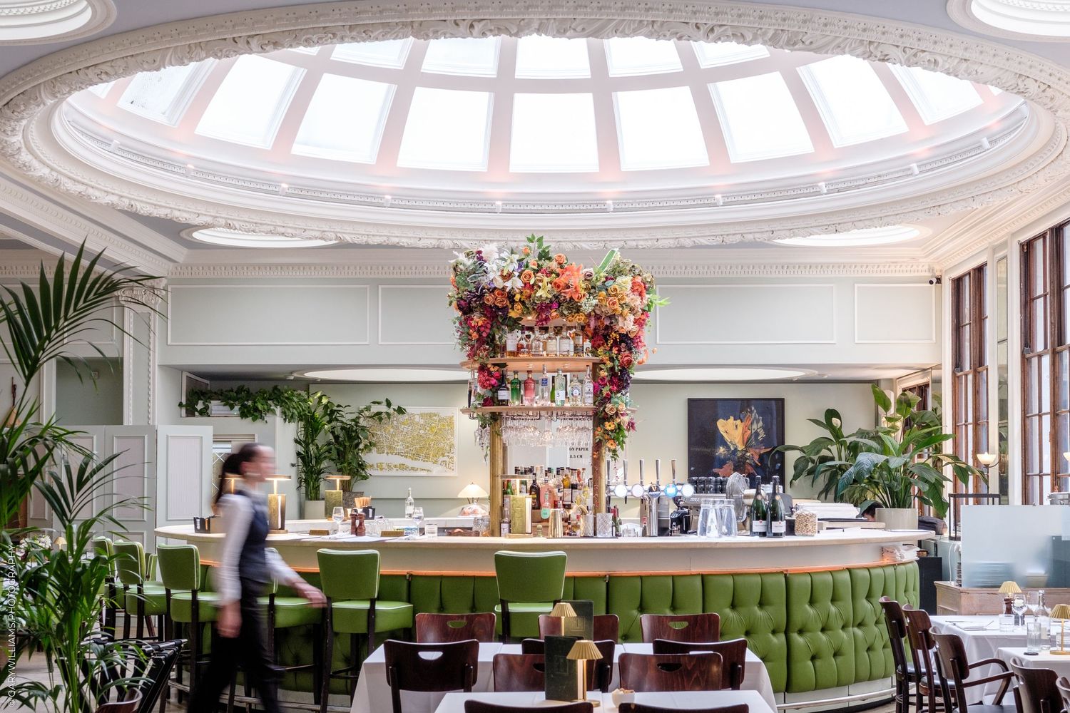 Elegant interior on 1 Lombard Street with green velvet seating, floral chandelier, and a curved bar under a domed skylight.