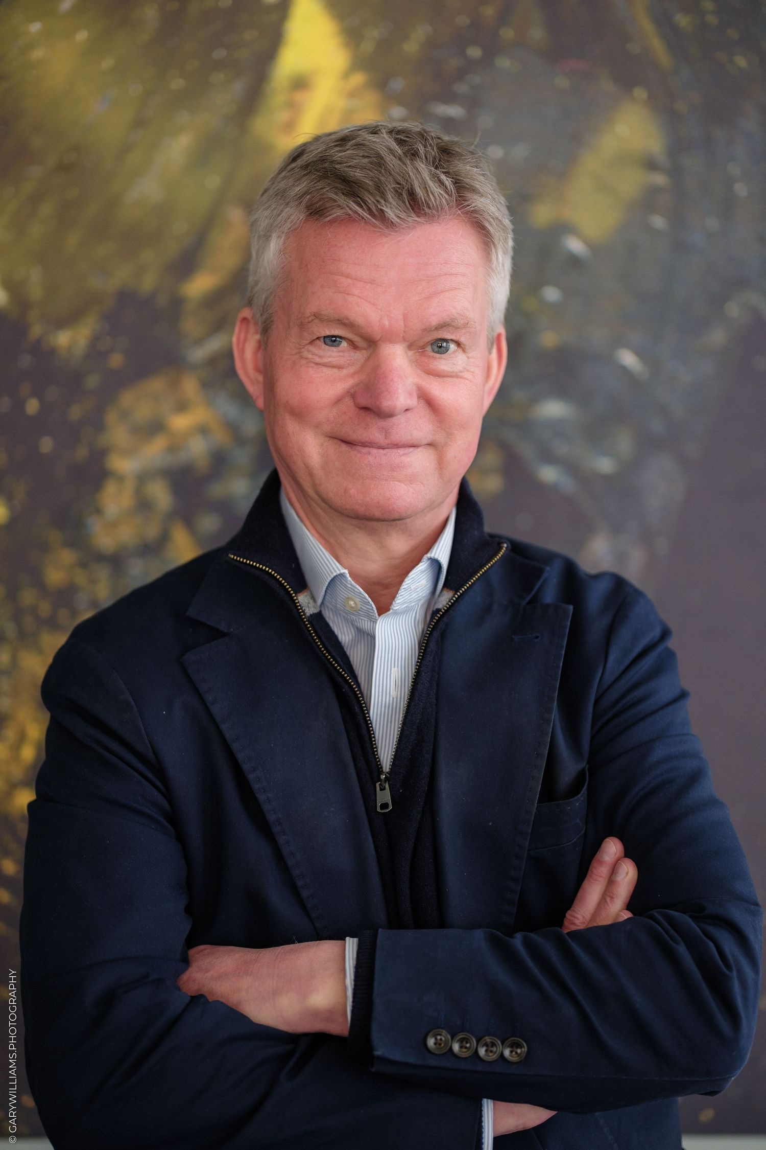 Soren Jessen wearing a navy blazer, smiling in front of an abstract painting.