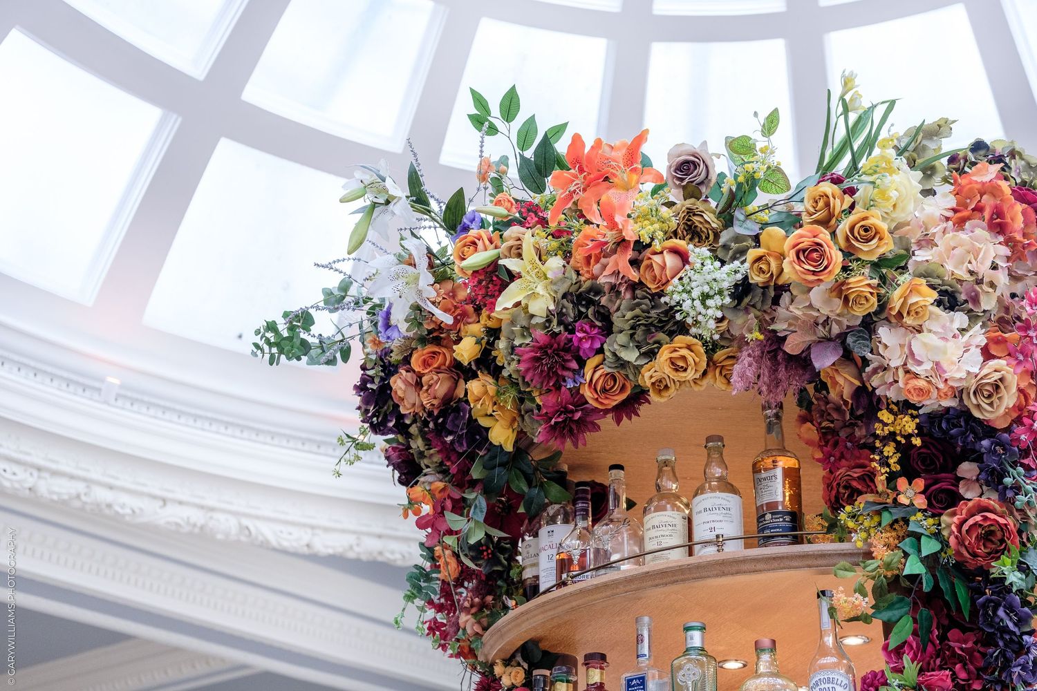 Lush floral arrangement of colorful roses and wildflowers adorning a tiered bar display under an elegant domed ceiling of 1 Lombard Street