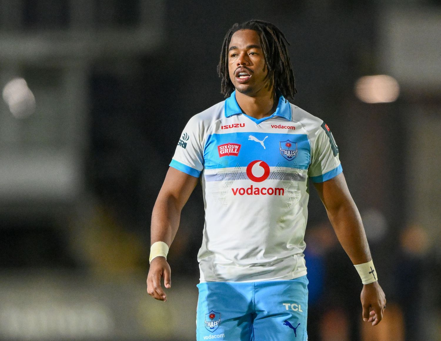 Rugby player in white Vodacom jersey on field during night match.