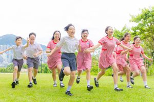 Happy children in school uniforms run and laugh together on a green lawn outdoors.
孩子們穿著校服，在戶外綠茵的草坪上快樂地奔跑、歡笑。