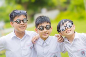 Three smiling Asian boys in white school uniforms wearing funny novelty glasses outdoors in a park.
三個身穿白色校服、戴著滑稽新奇眼鏡的亞裔男孩在公園裡微笑。