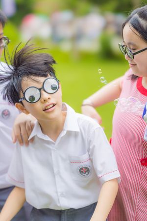 Children in school uniforms playing outdoors, boy wearing funny googly eye glasses, smiling and having fun.孩子們穿著校服在戶外玩耍，一個男孩戴著滑稽的卡通眼鏡，笑容燦爛。