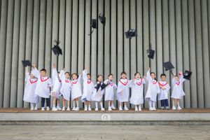 Children in graduation gowns tossing caps in the air outdoors, celebrating their kindergarten graduation ceremony.孩子們穿著畢業禮服，在戶外拋擲畢業帽，慶祝他們畢業