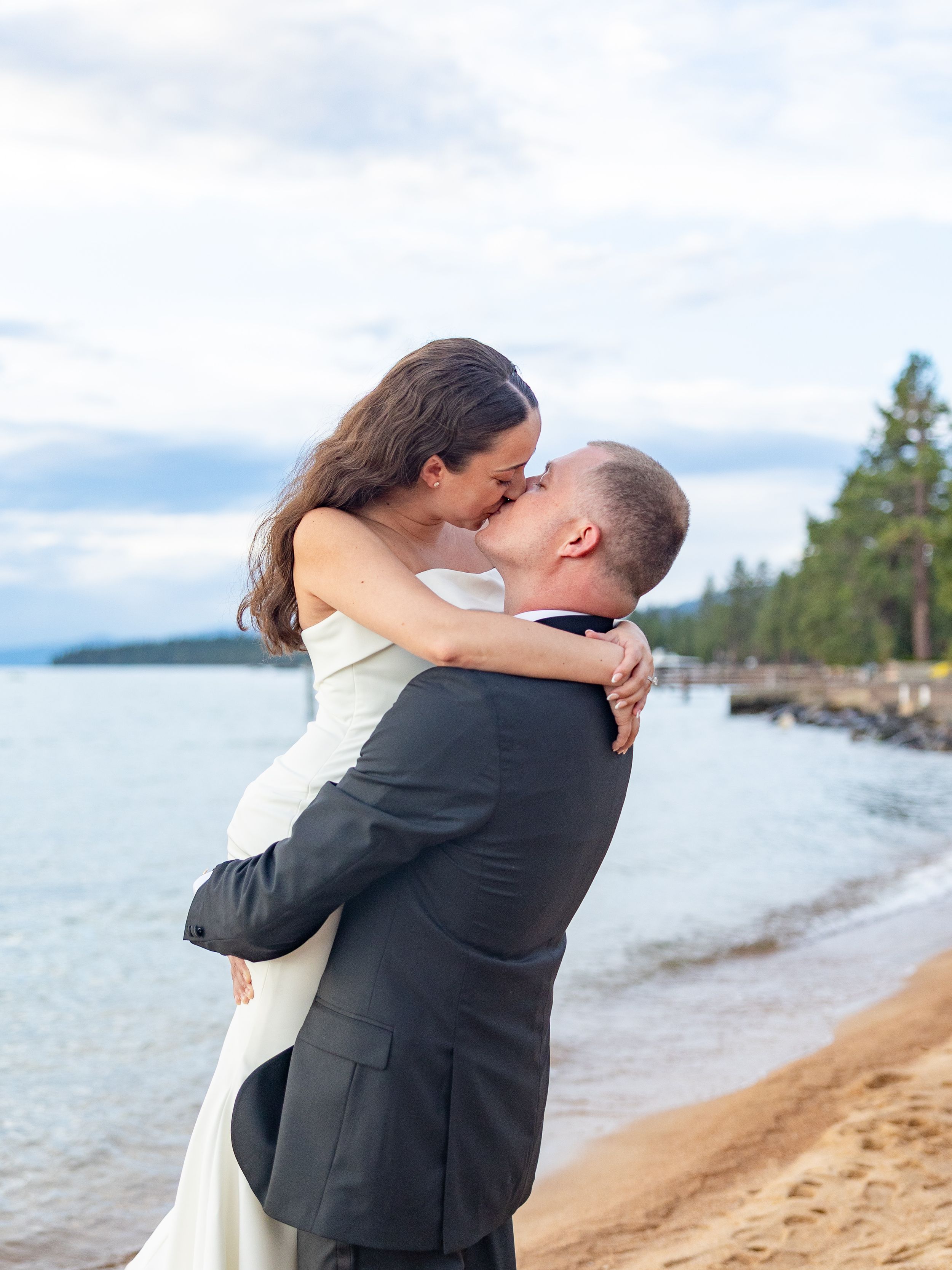 Newlyweds share a romantic kiss on a sandy Lake Tahoe beach after their wedding.
