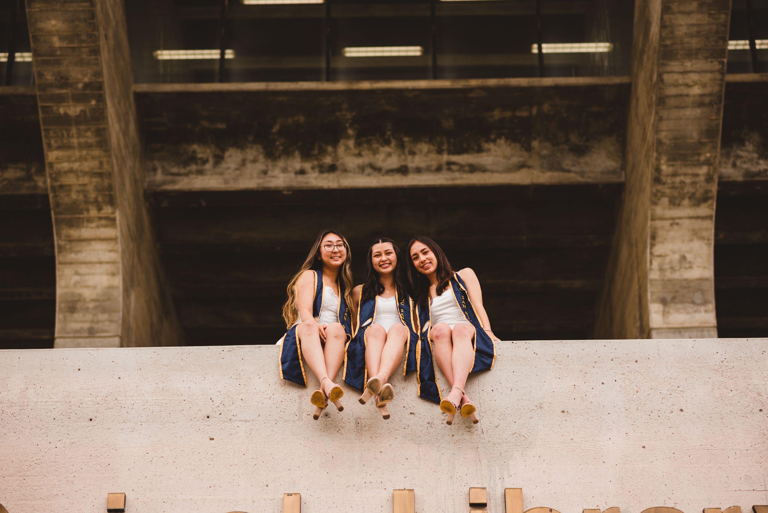 Three UCSD graduates posing for grad photos at Geisel Library.