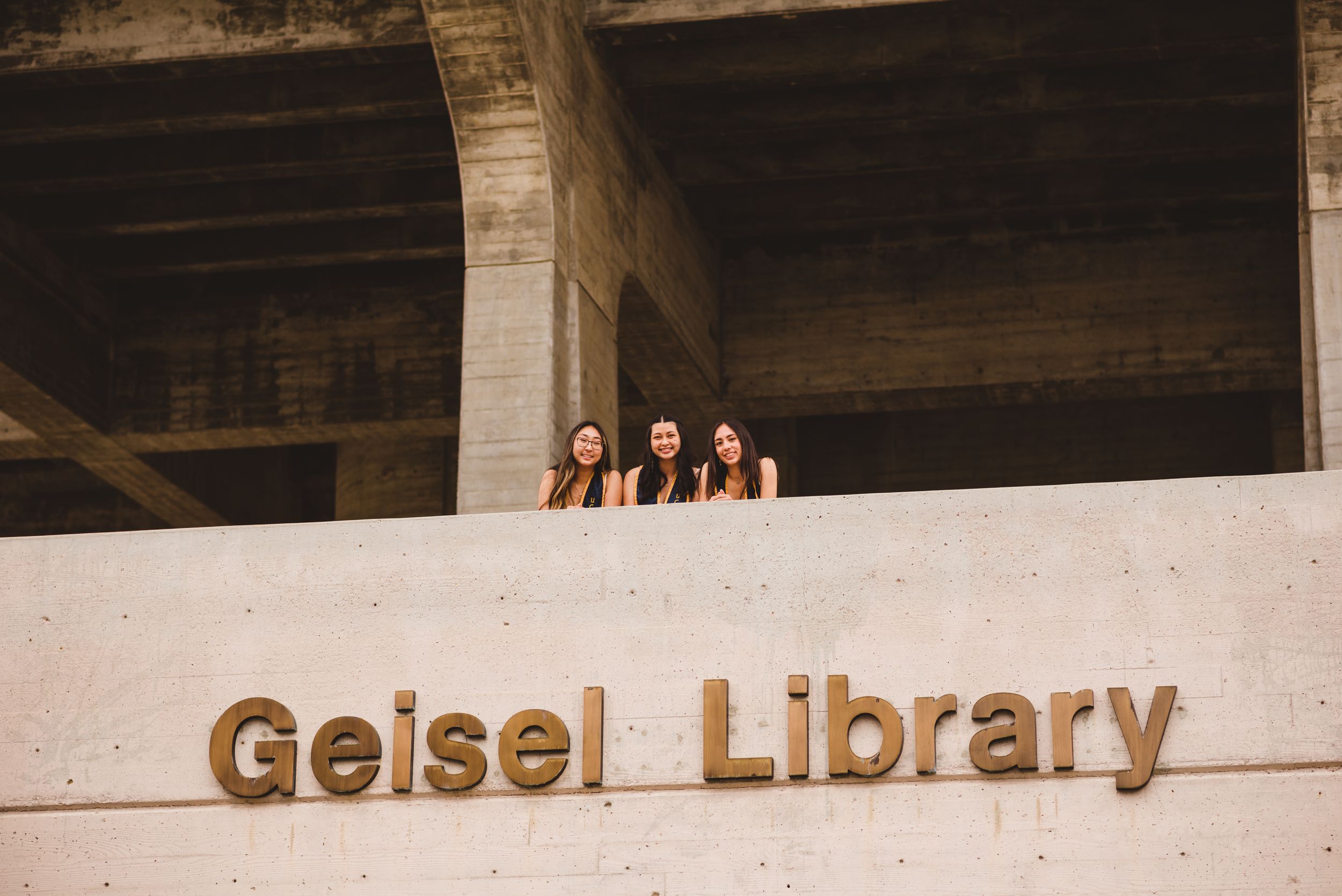 Three UCSD graduates posing for grad photos at Geisel Library.