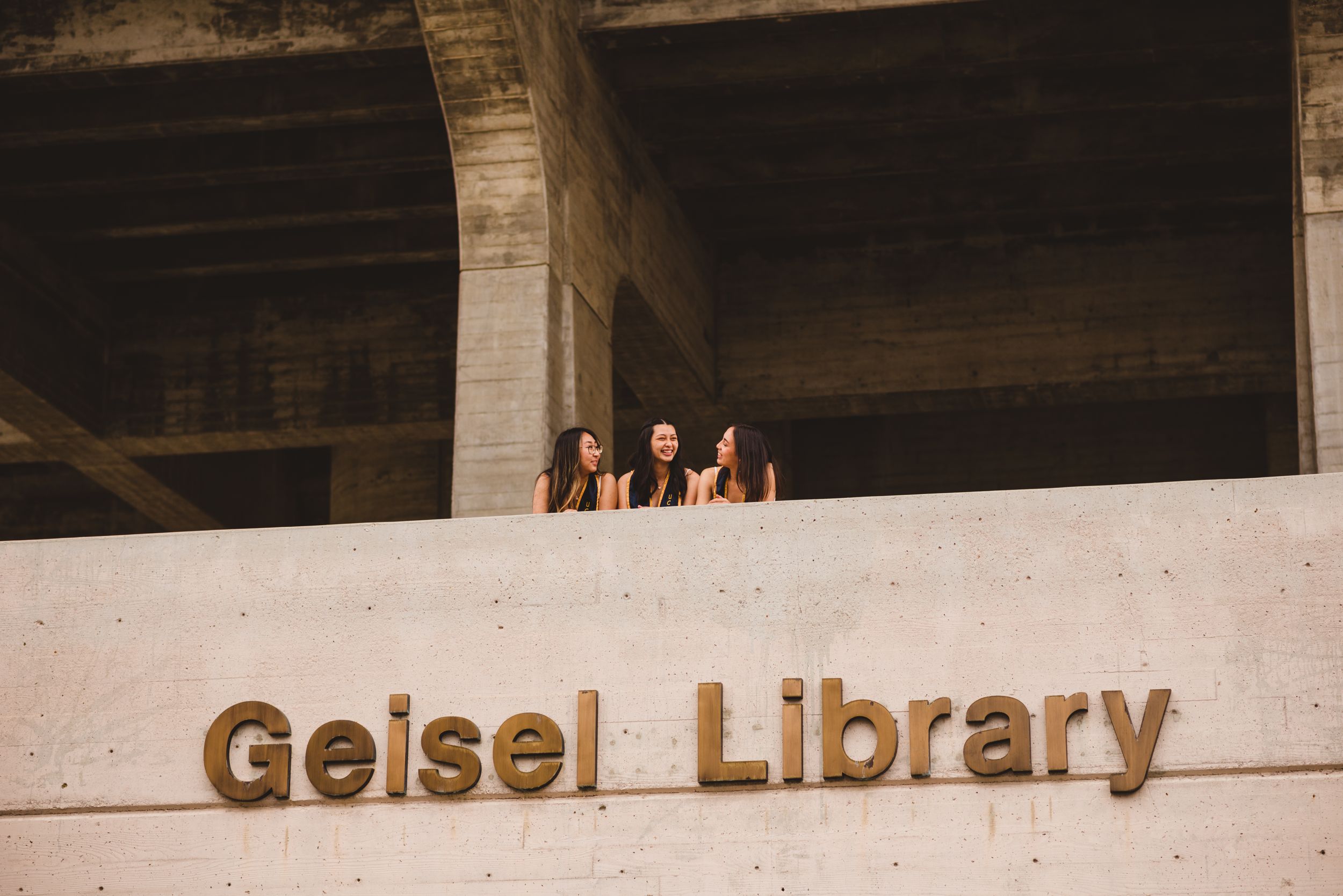 Three UCSD graduates posing for grad photos at Geisel Library.