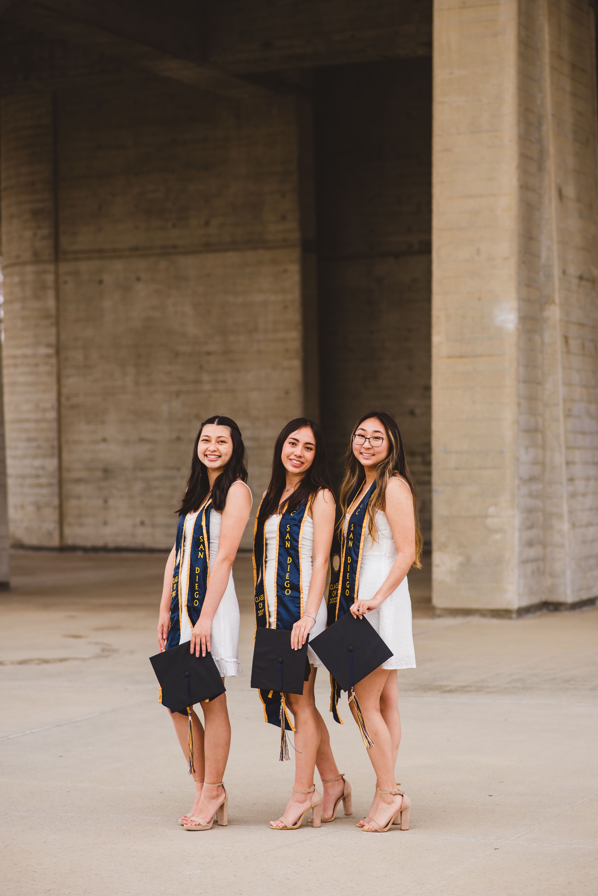 Three UCSD graduates posing for grad photos at Geisel Library.