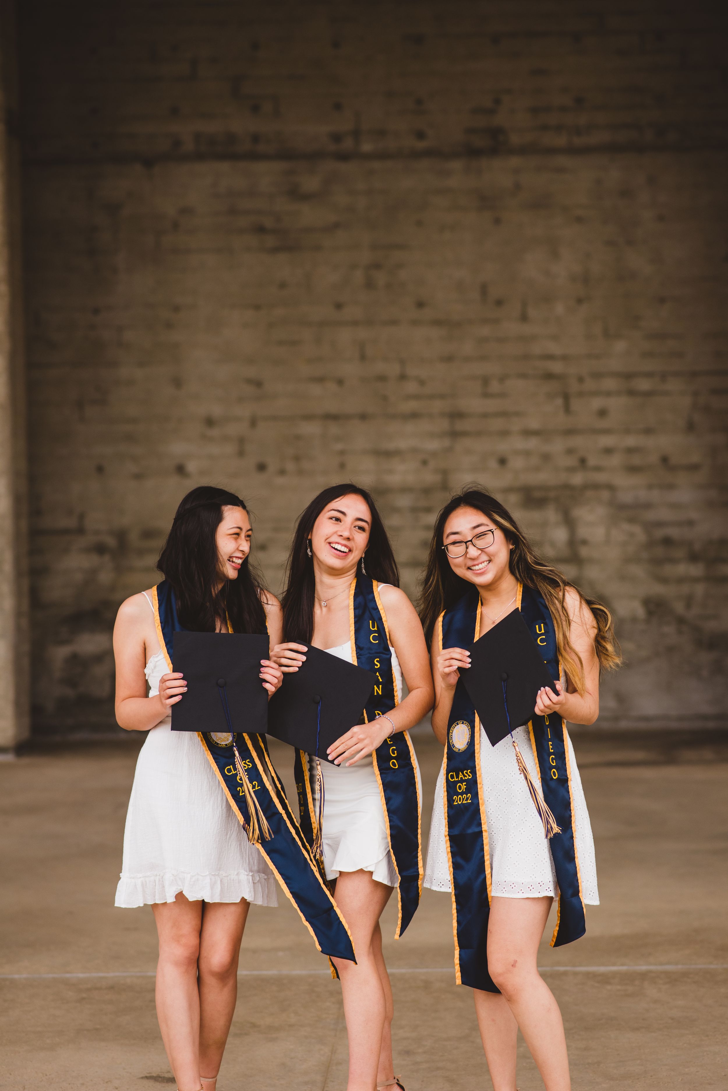 Three UCSD graduates posing for grad photos at Geisel Library.