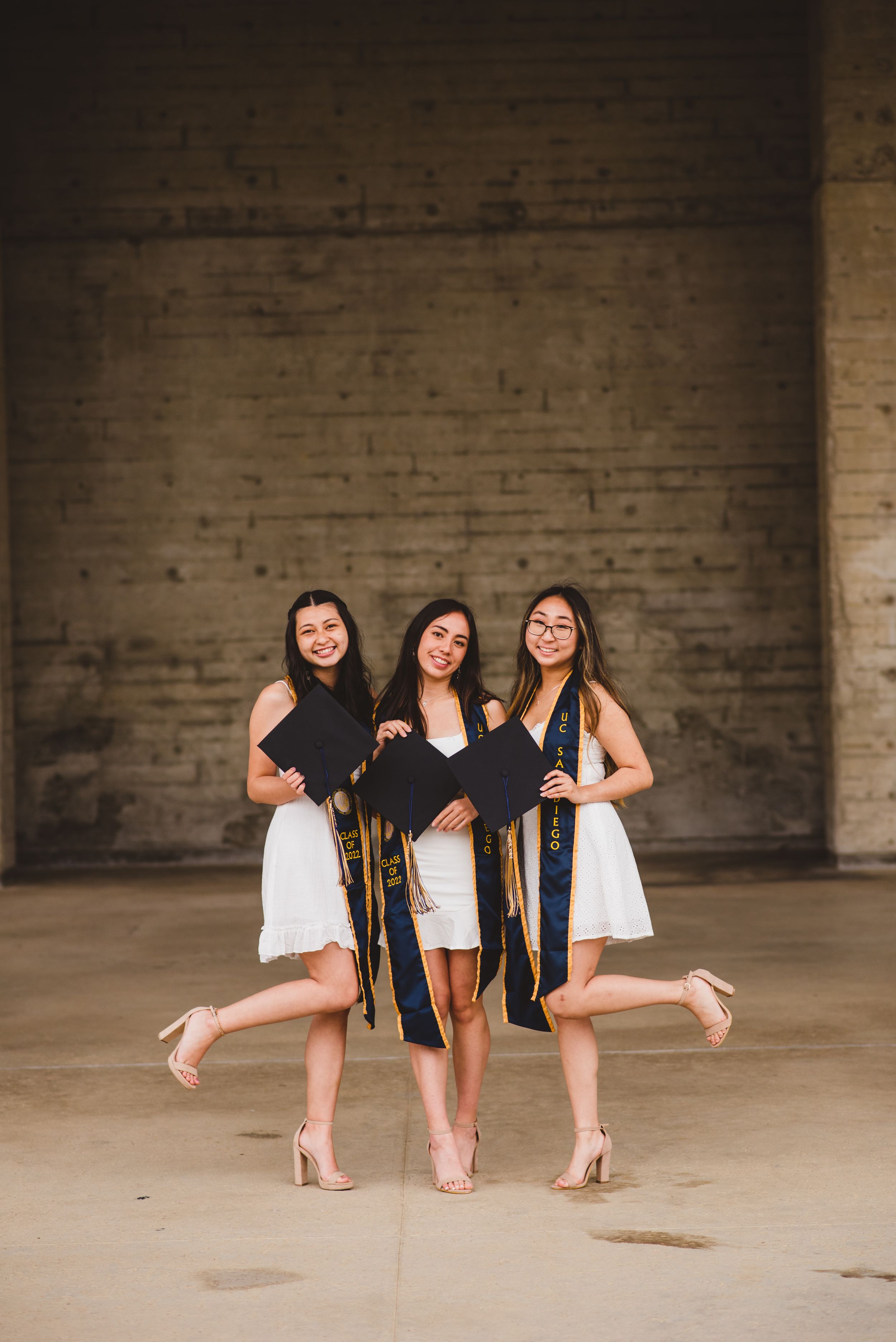 Three UCSD graduates posing for grad photos at Geisel Library.