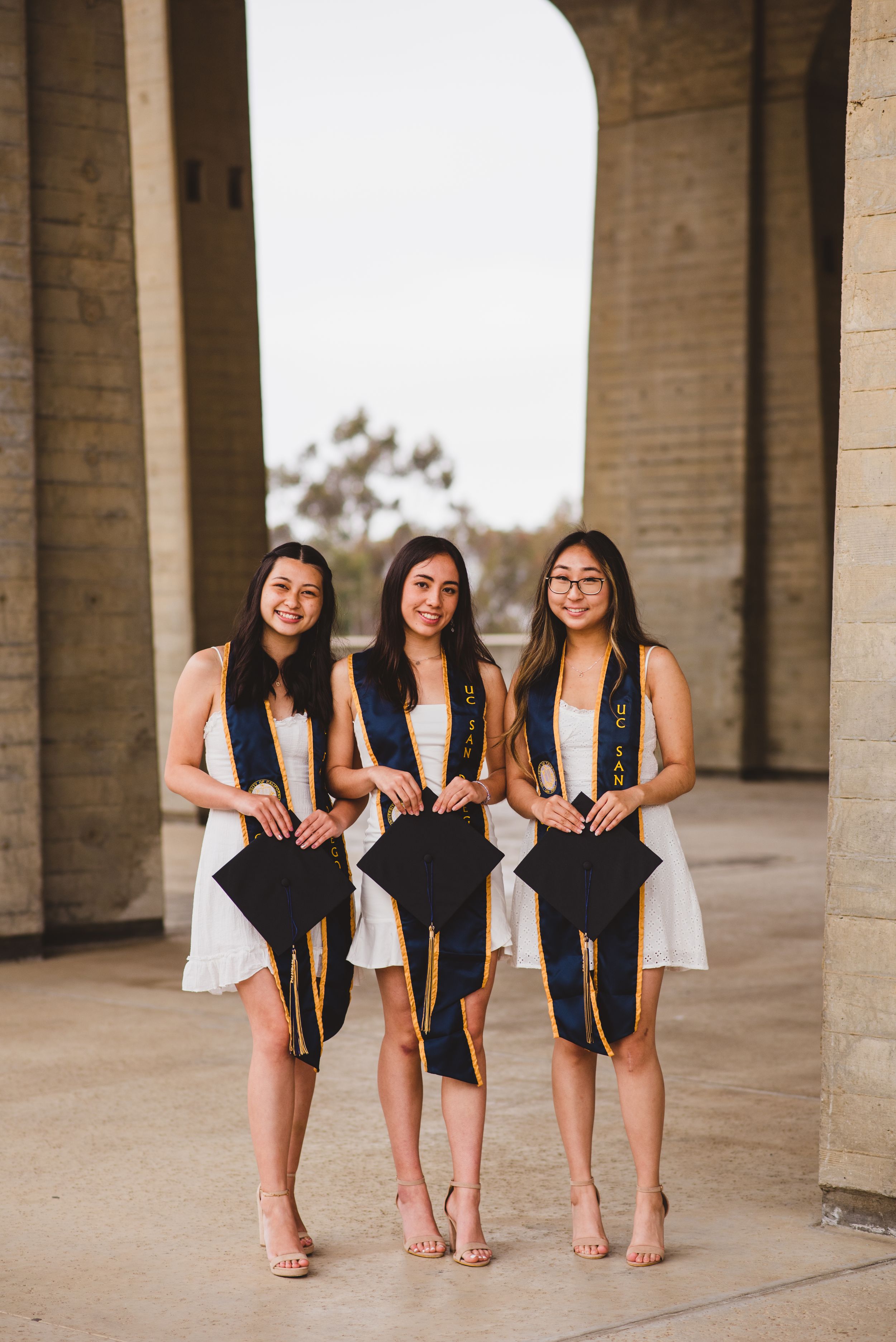 Three UCSD graduates posing for grad photos at Geisel Library.