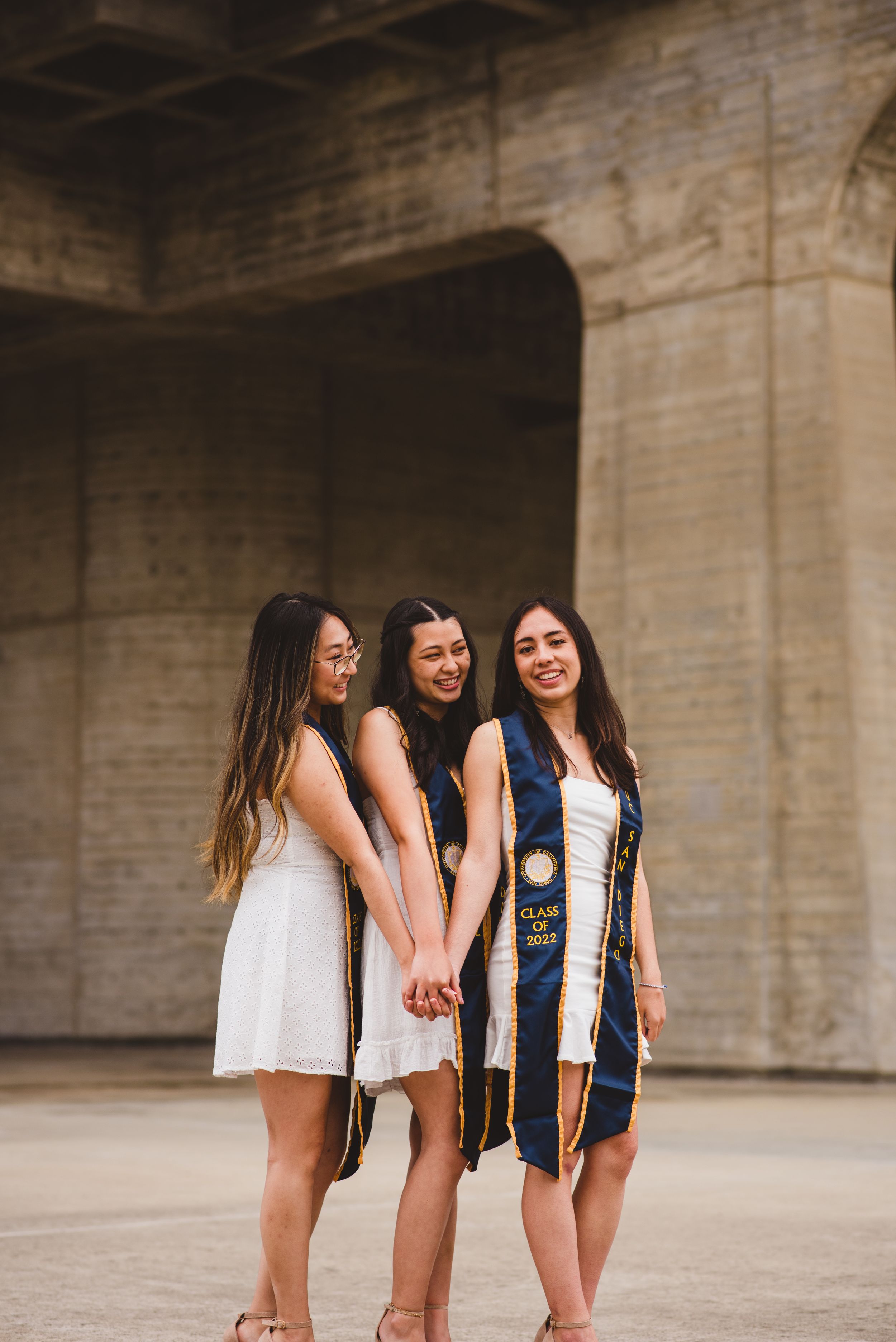Three UCSD graduates posing for grad photos at Geisel Library.
