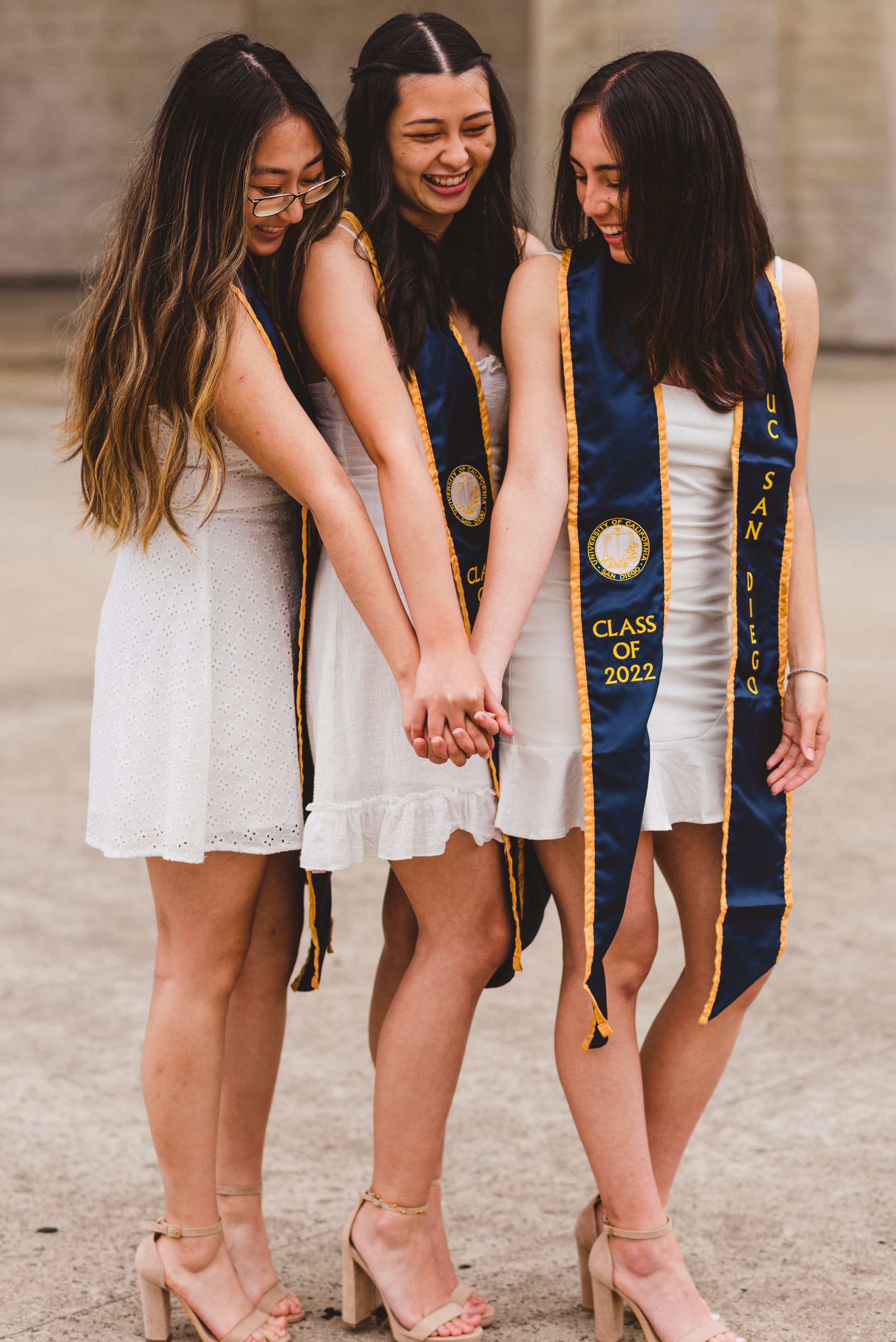 Three UCSD graduates holding hands and posing for grad photos at Geisel Library.