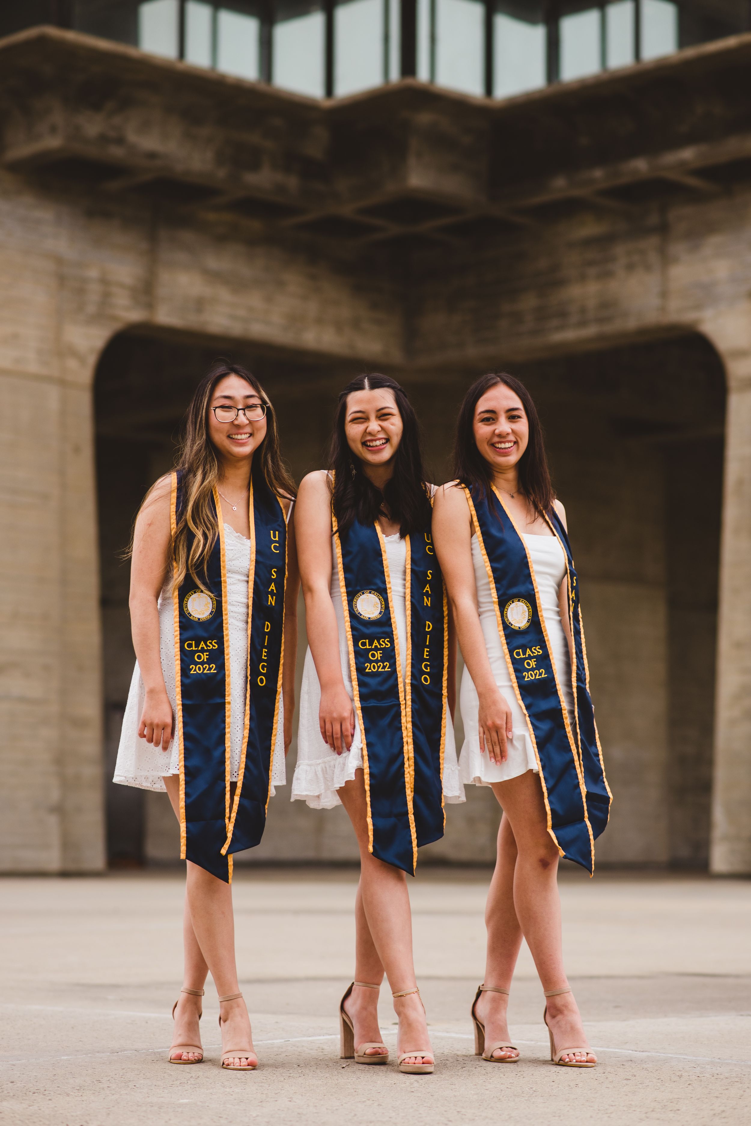 Three UCSD graduates posing for grad photos at Geisel Library.
