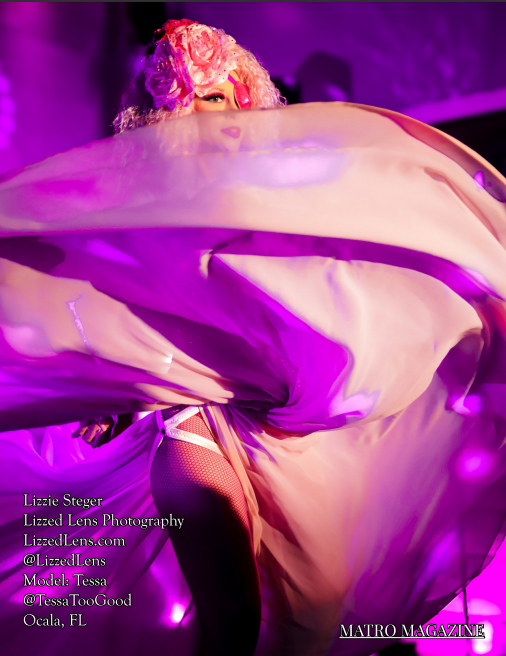 Performer in pink floral headpiece twirling white and purple fabric under stage lighting.