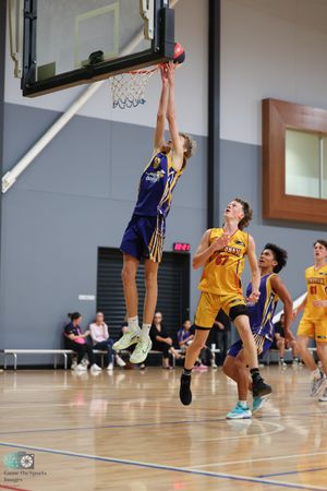 Basketball player in blue jersey reaches high to score at the basket while yellow opponents defend.