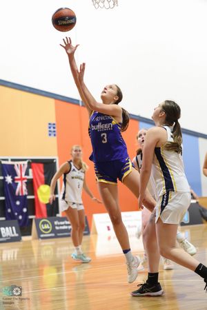 Basketball player in purple jersey reaches for layup during competitive game.