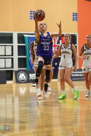 Player in purple jersey drives toward basket for layup during basketball game.