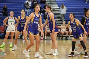 Basketball teams in purple and white uniforms stand on court during game break.
