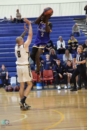 Player in blue jersey takes a jump shot over defender in white during basketball game.