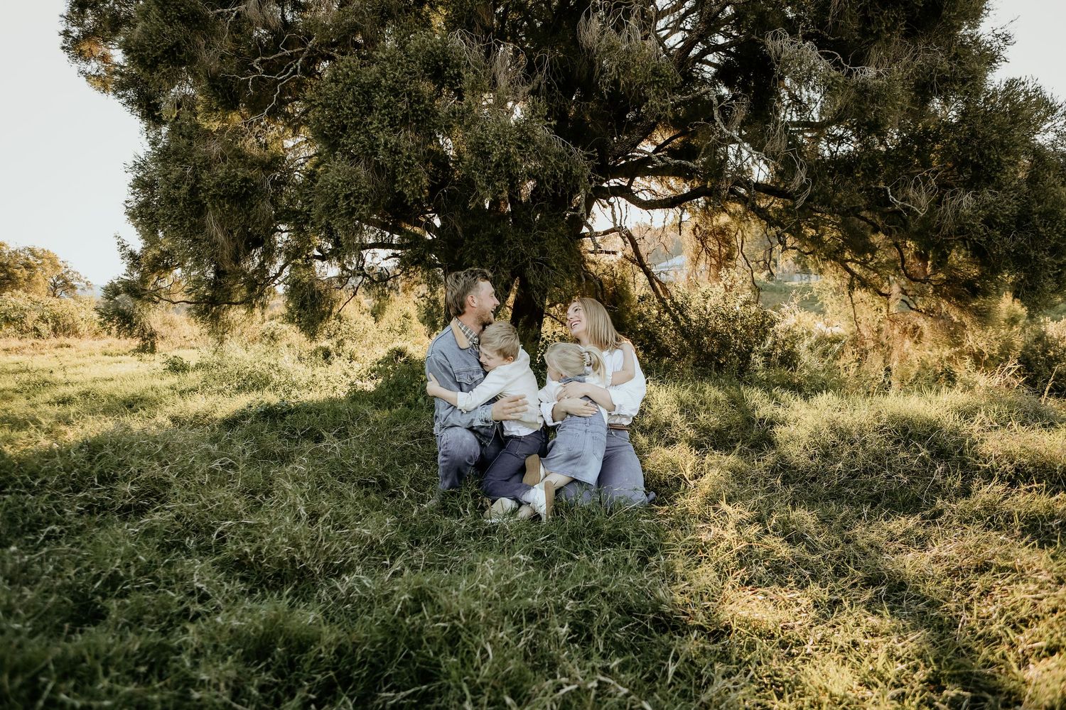 People sit together on a grassy hillside during golden hour as sunlight filters through trees.