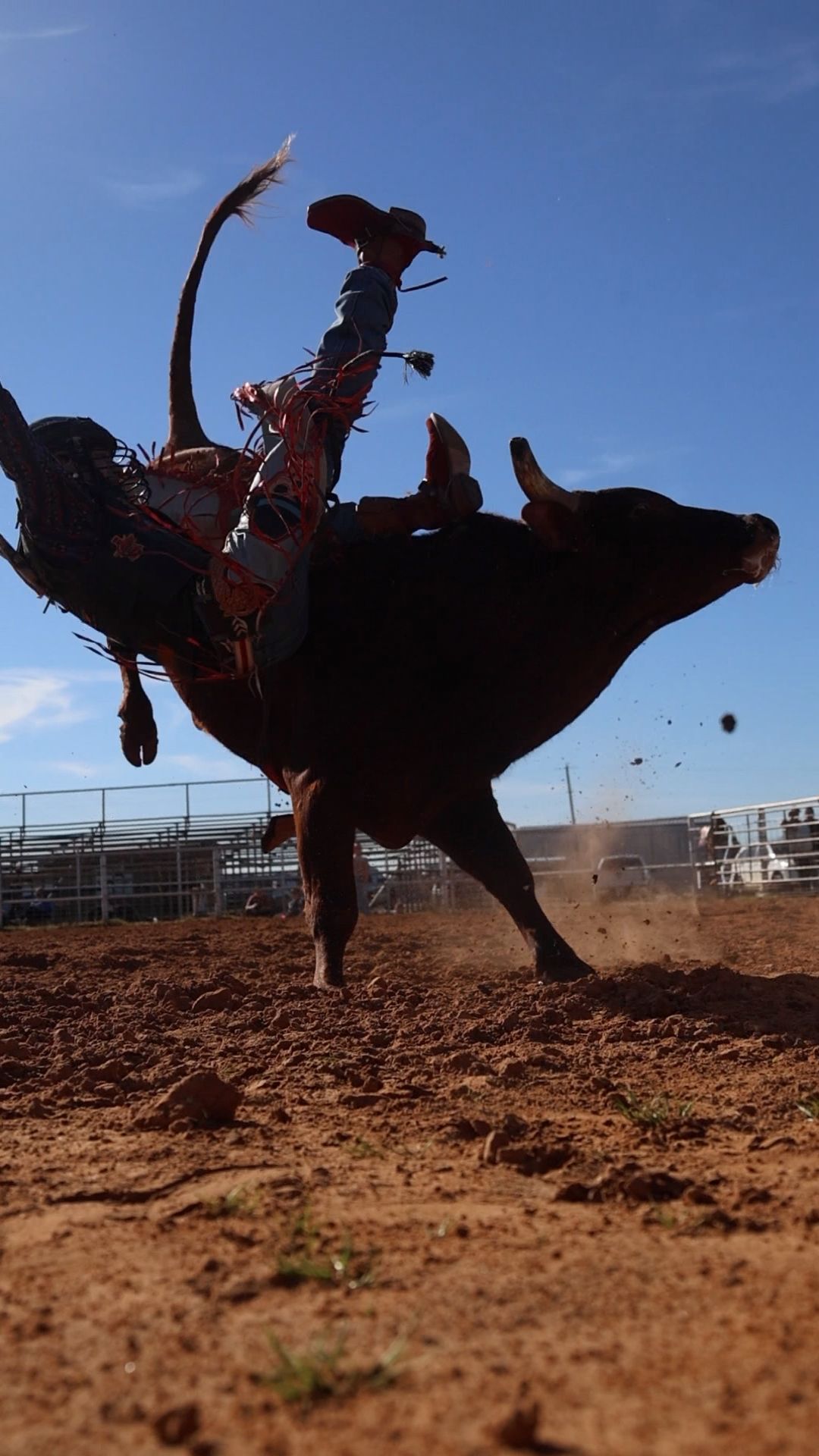 A rodeo rider at a country western event performs a trick while holding onto a moving horse at an outdoor arena.