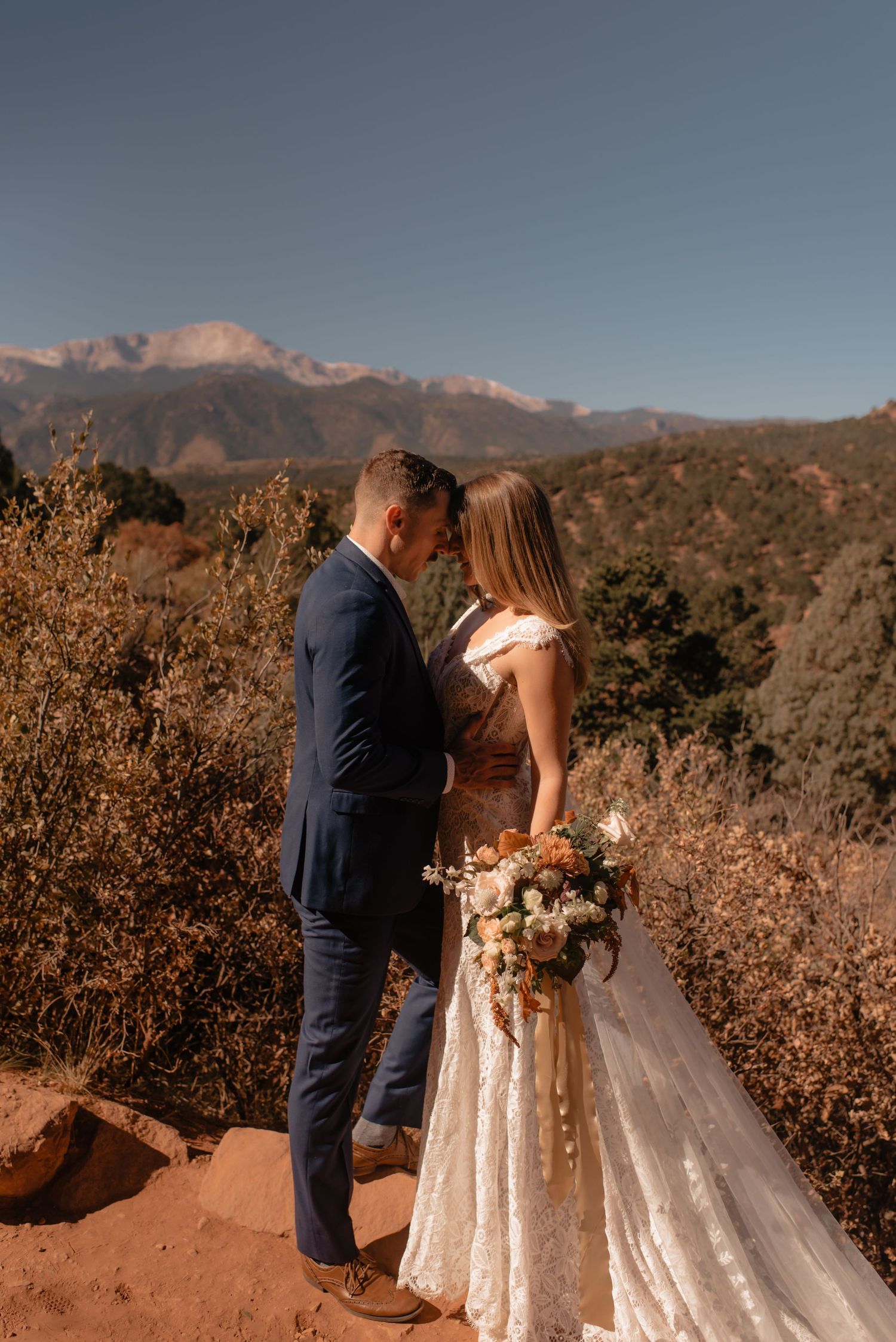 Wedding couple embraces against mountain backdrop at Garden of the Gods during golden hour sunset.