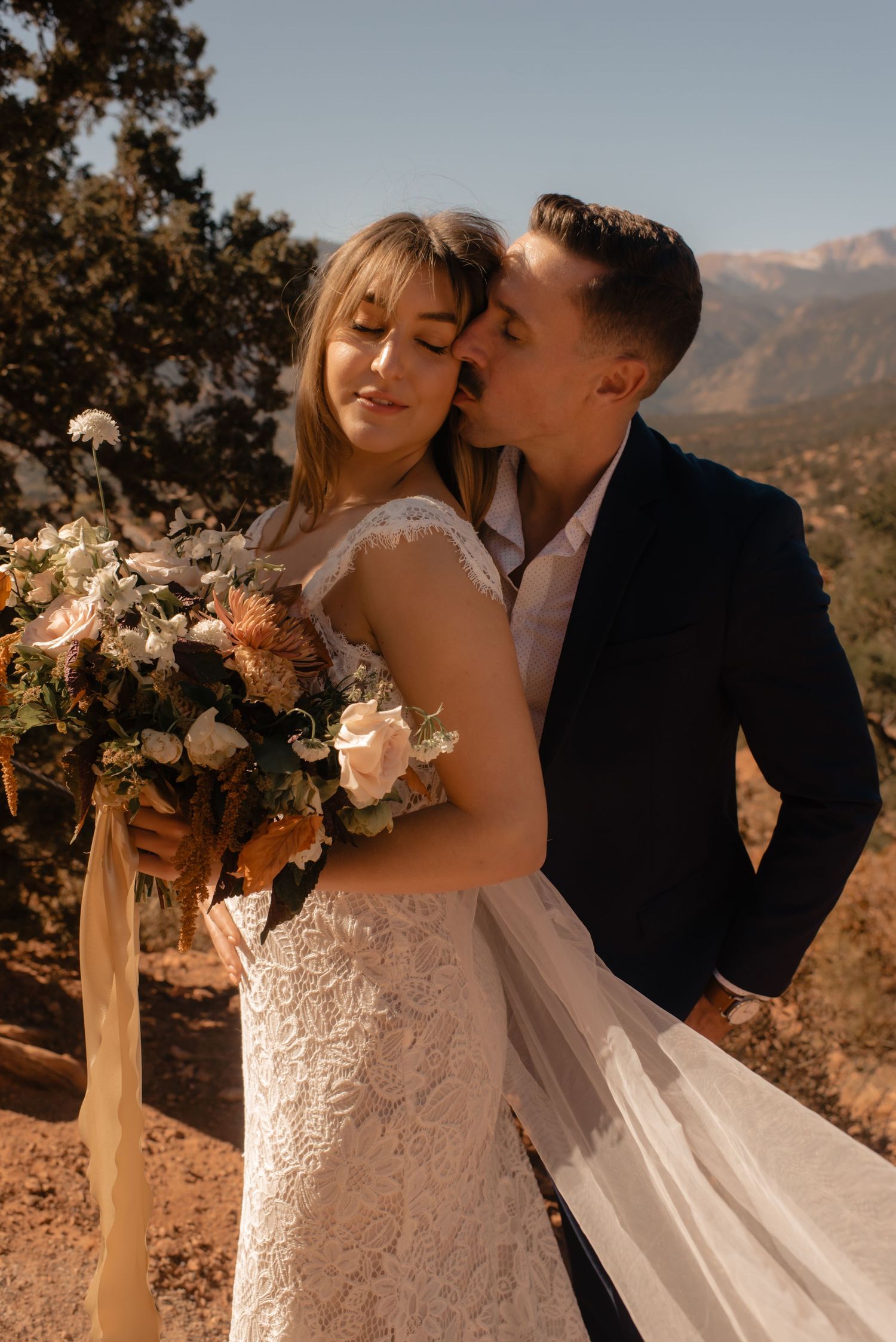 A romantic wedding couple stands on a mountain overlook at sunset with a beautiful autumn bouquet.