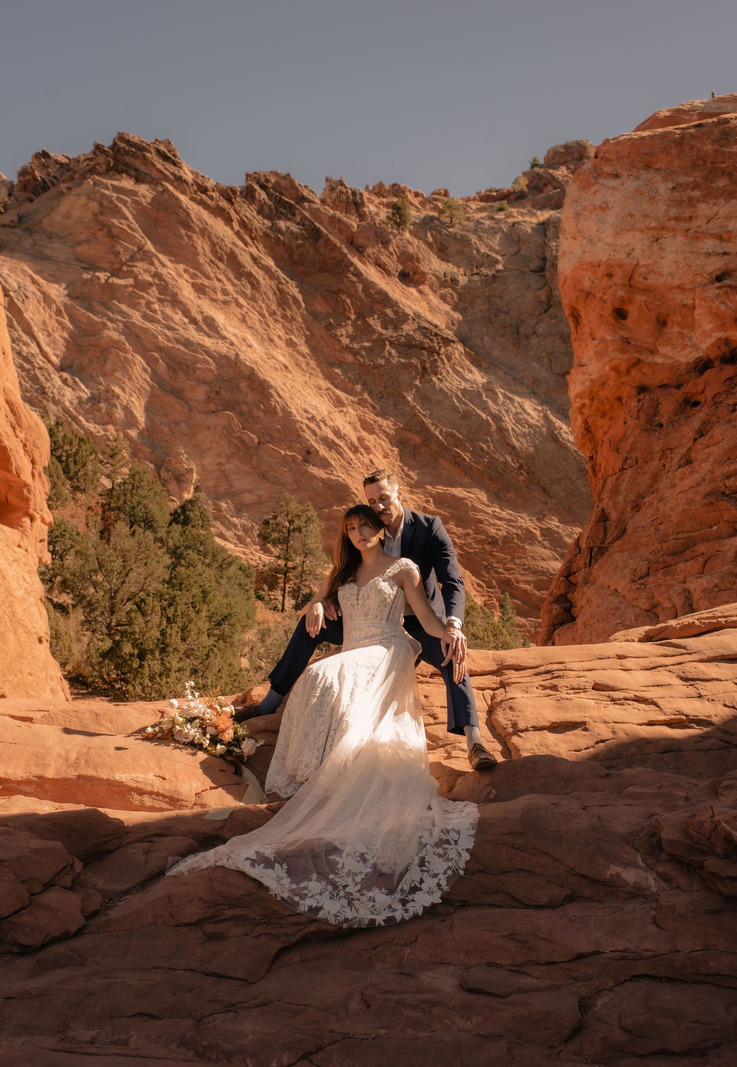 A couple in wedding attire sits together on red rock formations during sunset at Valley of Fire State Park.