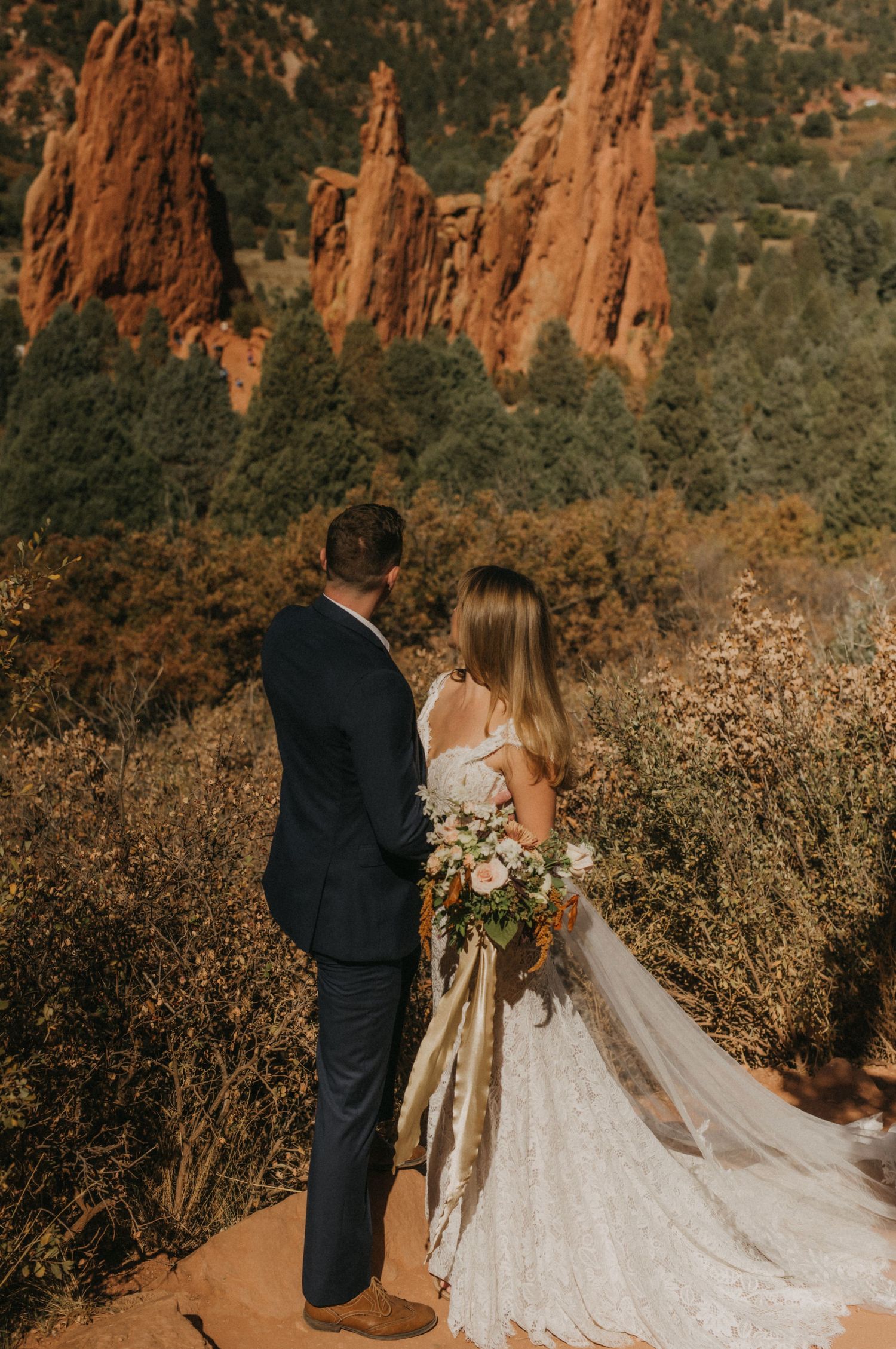 A couple in wedding attire poses against the scenic red rock formations of Garden of the Gods in Colorado.