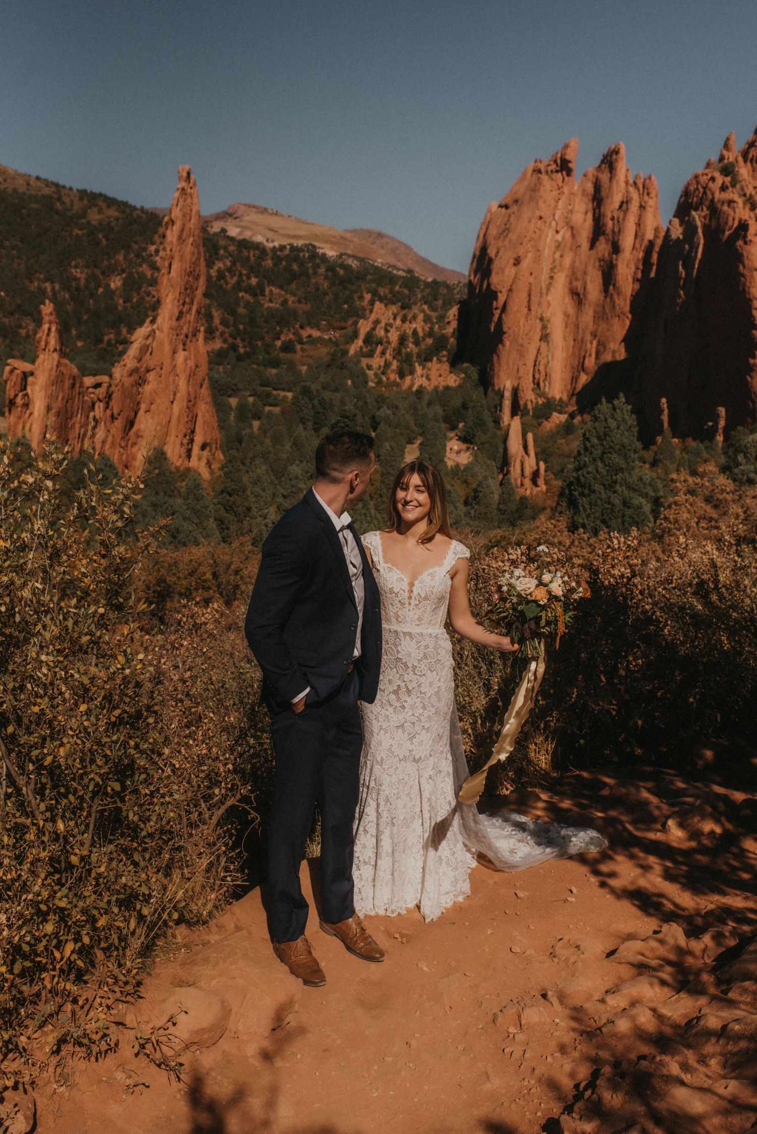 A wedding couple poses against stunning red rock formations at Garden of the Gods during golden hour.