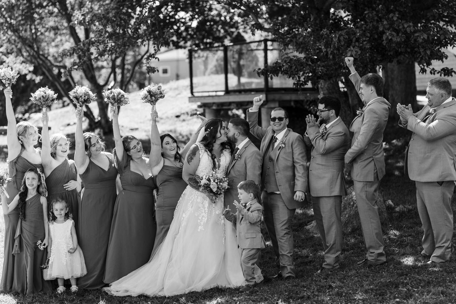 A wedding party poses together outdoors in black and white, with ladies in long dresses and men in suits.