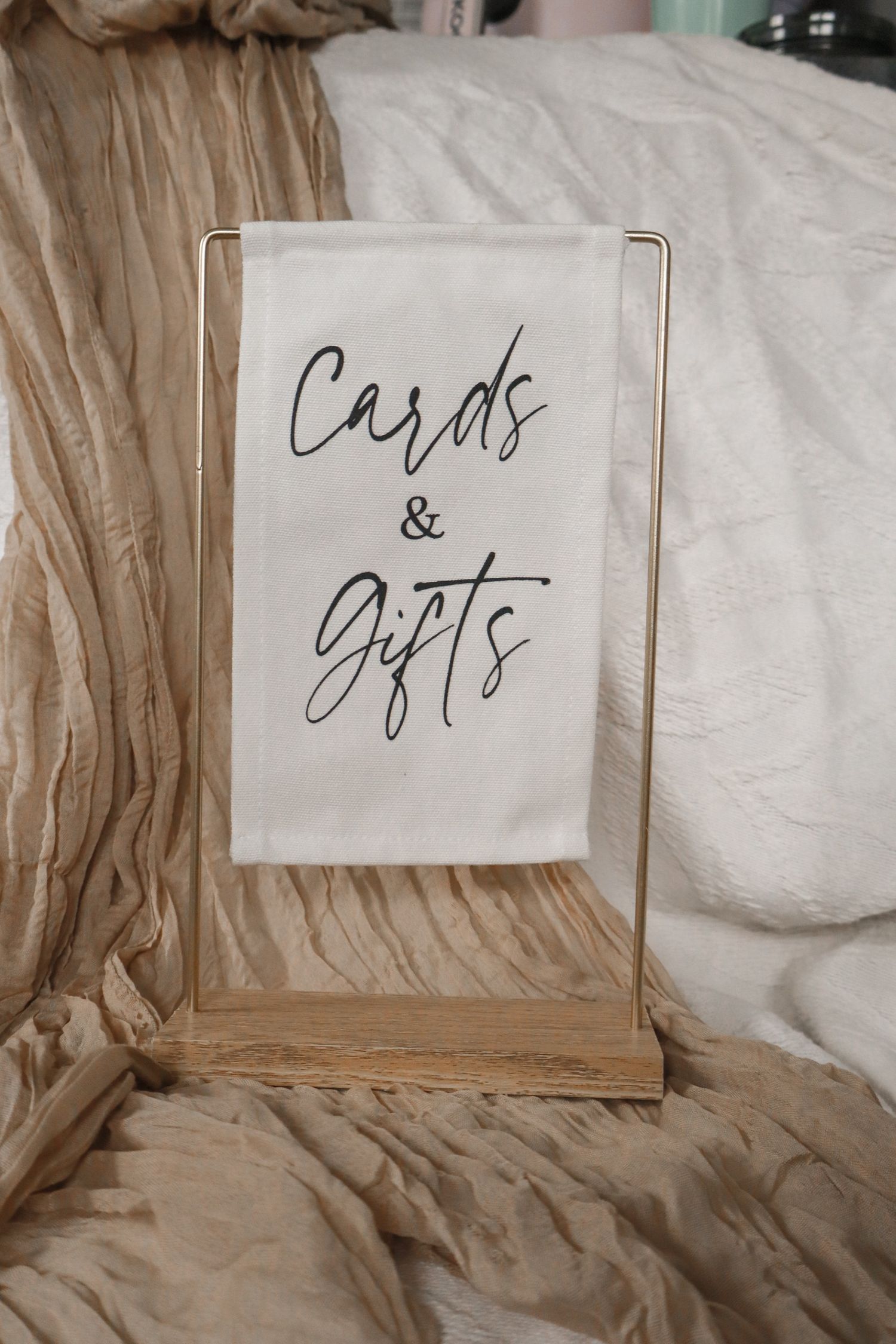 A wedding 'Cards & Gifts' sign with dried pampas grass and floral decorations displayed on a woven rattan table outdoors.