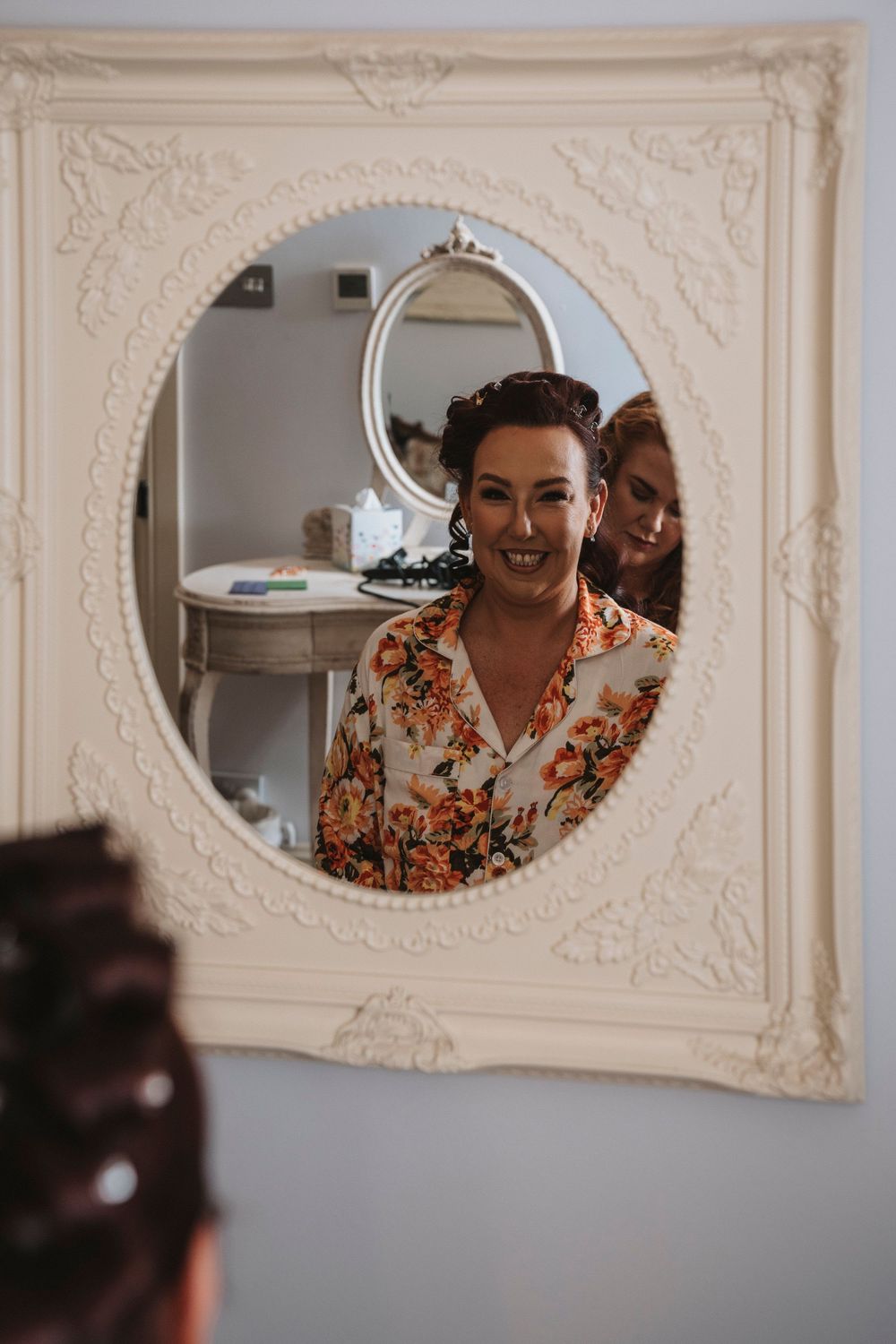 Mirror reflection shows person in floral print top framed by detailed white wall moldings ornate architecture.