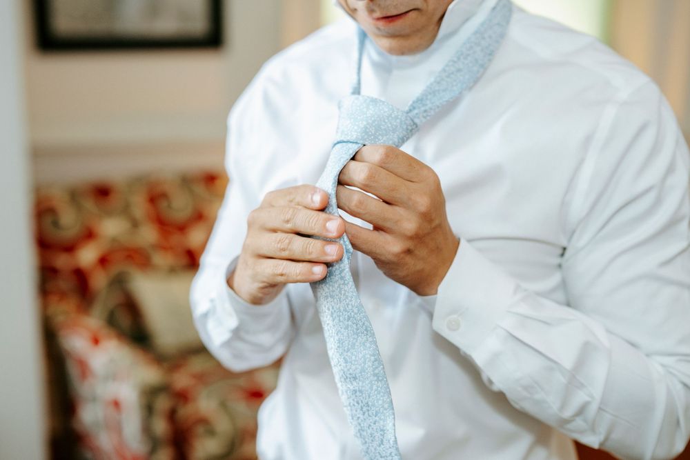 Someone adjusts a light blue necktie while getting ready for a formal event.