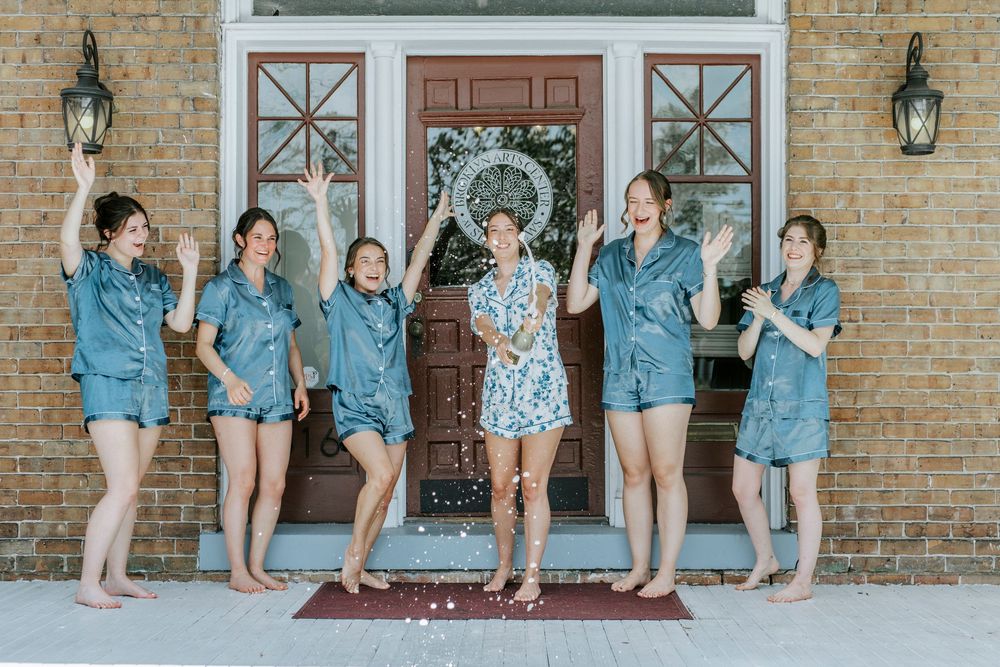 Bridesmaids in matching blue denim outfits pose playfully on brick steps.
