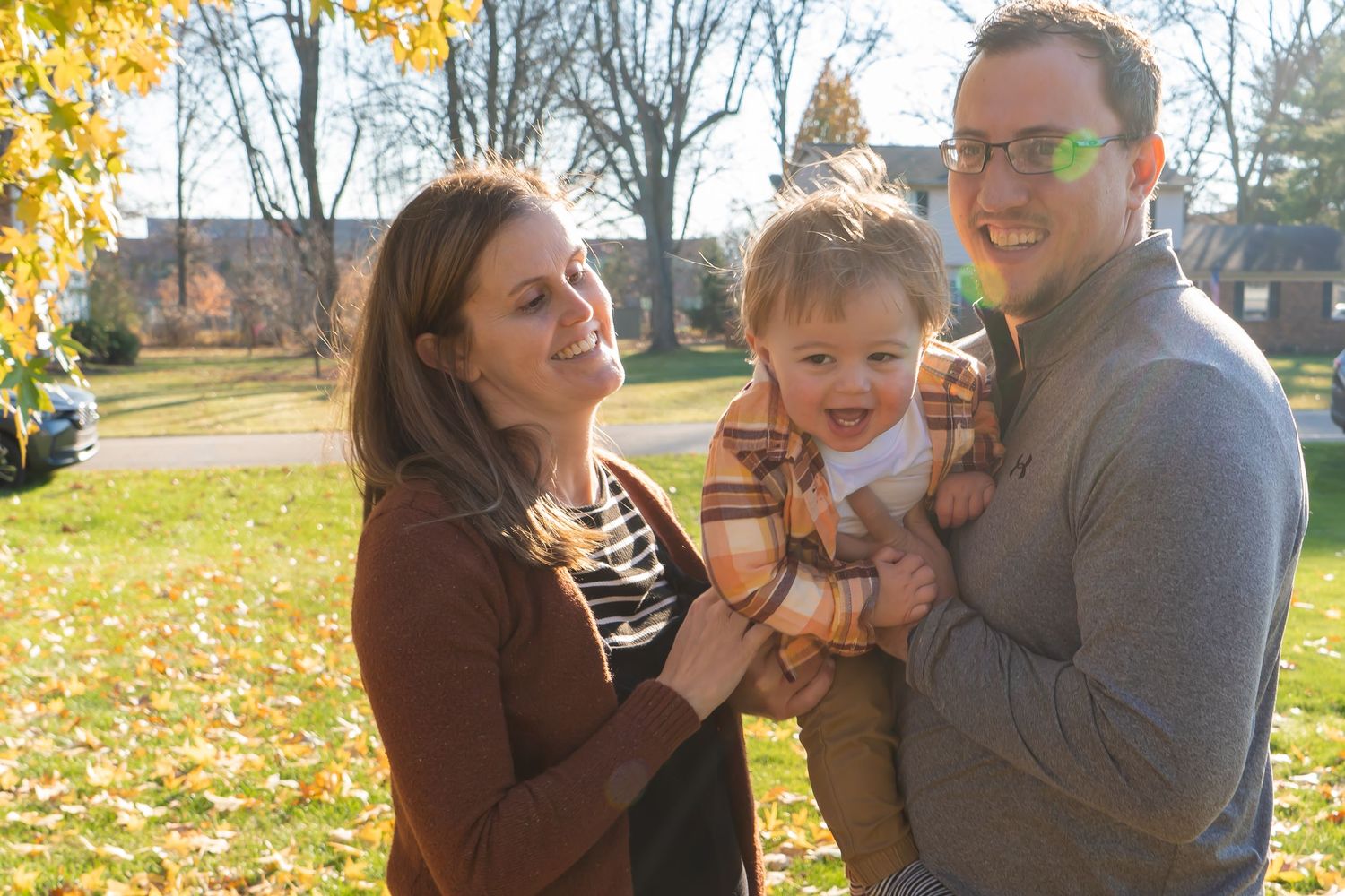A family stands together on a grassy lawn near evergreen trees in coordinating brown and blue outfits.