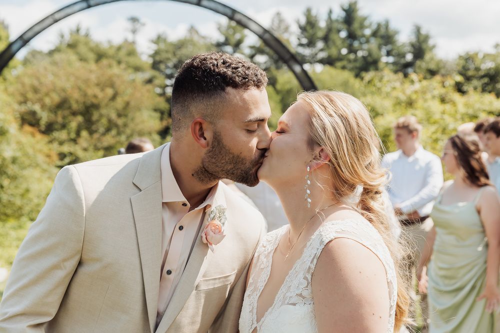 A happy couple shares intimate moments at their outdoor wedding celebration surrounded by guests and greenery.