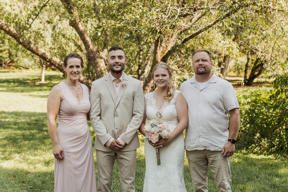 Wedding party poses outdoors in coordinated light beige and blush pink attire in a sunlit garden setting.